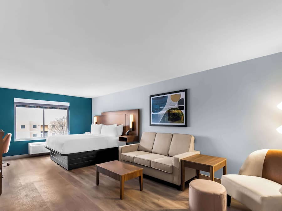A modern hotel room with a bed, sofa, coffee table, and a desk.