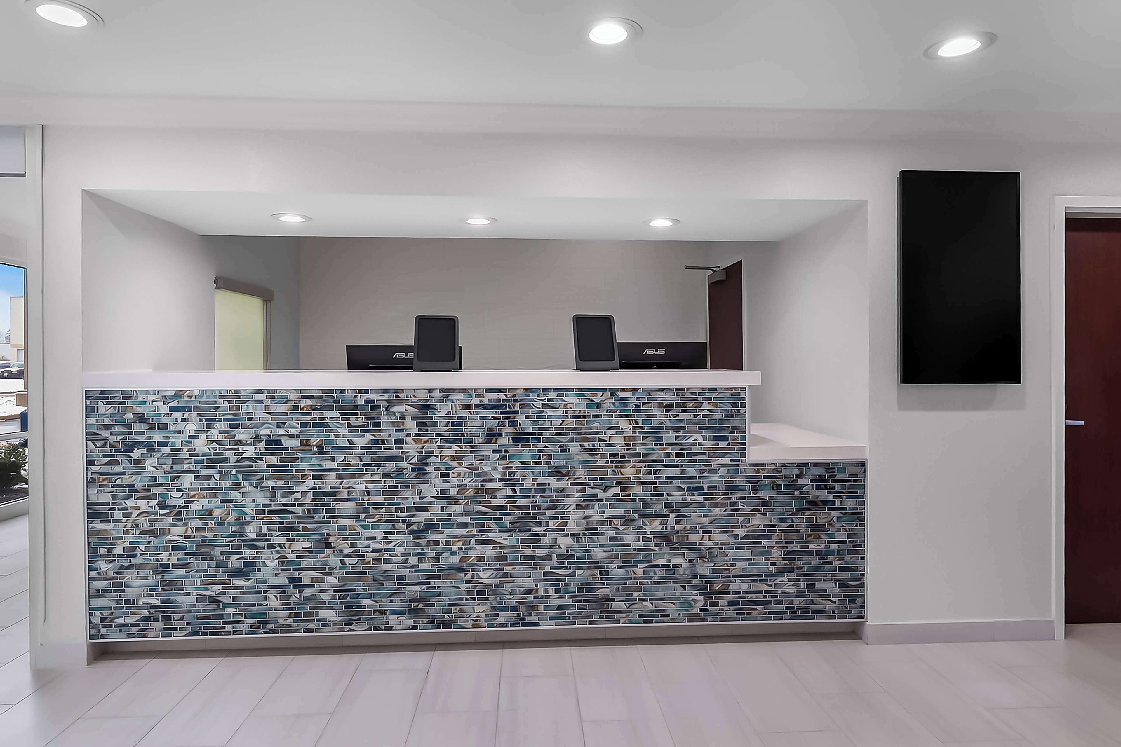 A reception area with a tiled wall, two black speakers, and a flat-screen TV mounted on the wall.
