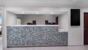 Un área de recepción con pared de azulejos, dos parlantes negros y un televisor de pantalla plana montado en la pared.
