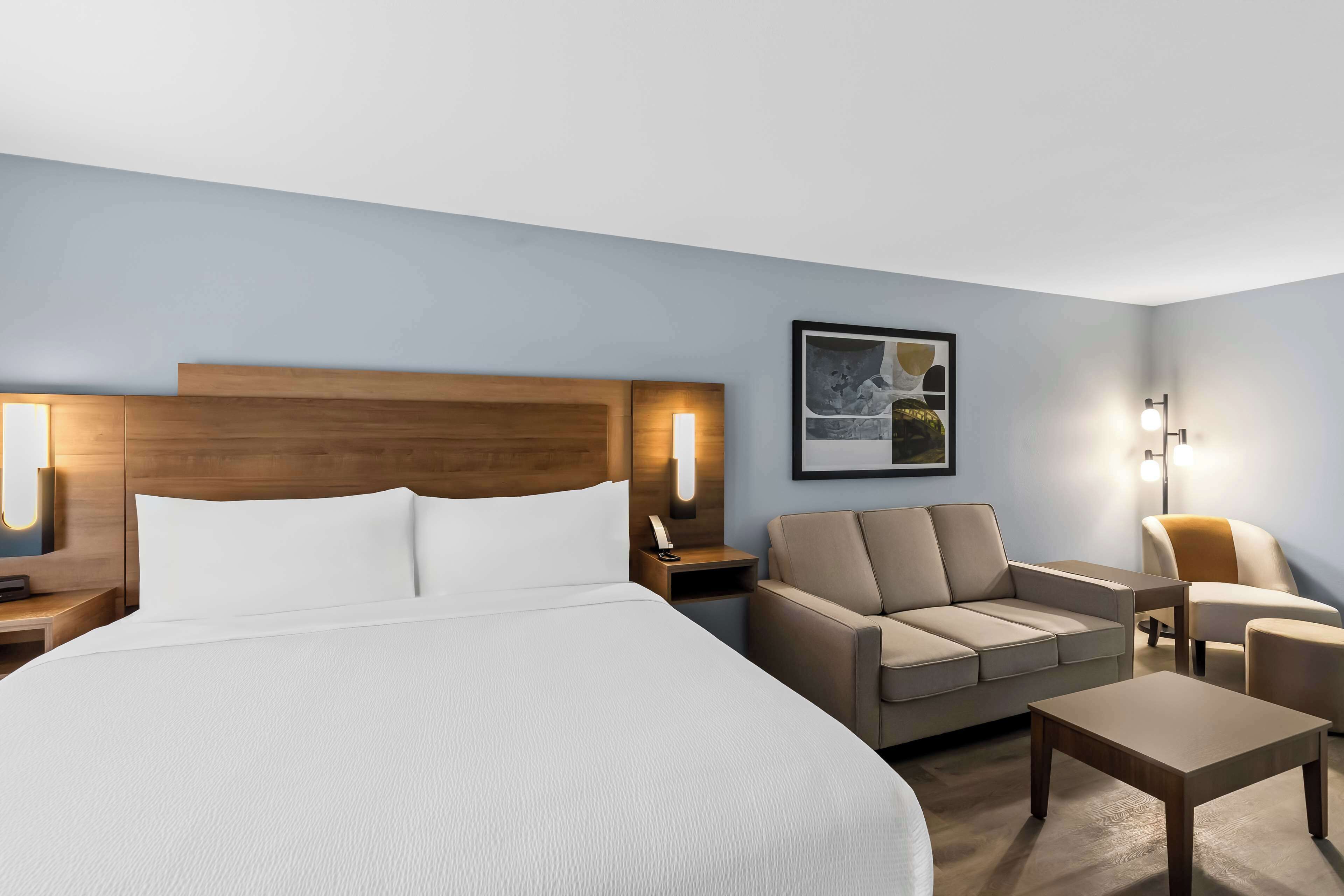 A hotel room with a large bed, a sofa, a small table, and two wall-mounted lamps.