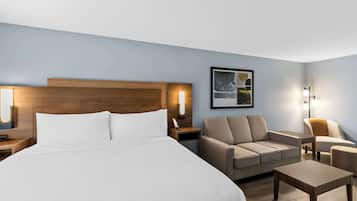 A hotel room with a large bed, a sofa, a small table, and two wall-mounted lamps.