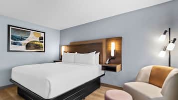 Ein modernes Hotelzimmer mit einem großen Bett, einem Holz-Kopfteil, einem Nachttisch mit Lampe und einem an der Wand befestigten Kunstwerk.