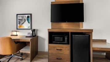 Ein kompakter Raum mit einem Holzbüro, einem schwarzen Kühlschrank, einer Mikrowelle und einem an einem Holzkasten montierten Fernseher.
