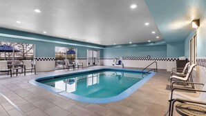 Una piscina interior con suelo de baldosas, una escalera de piscina y sillones de descanso.