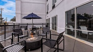 Un patio al aire libre con una chimenea, sillas de metal negro y un paraguas azul.