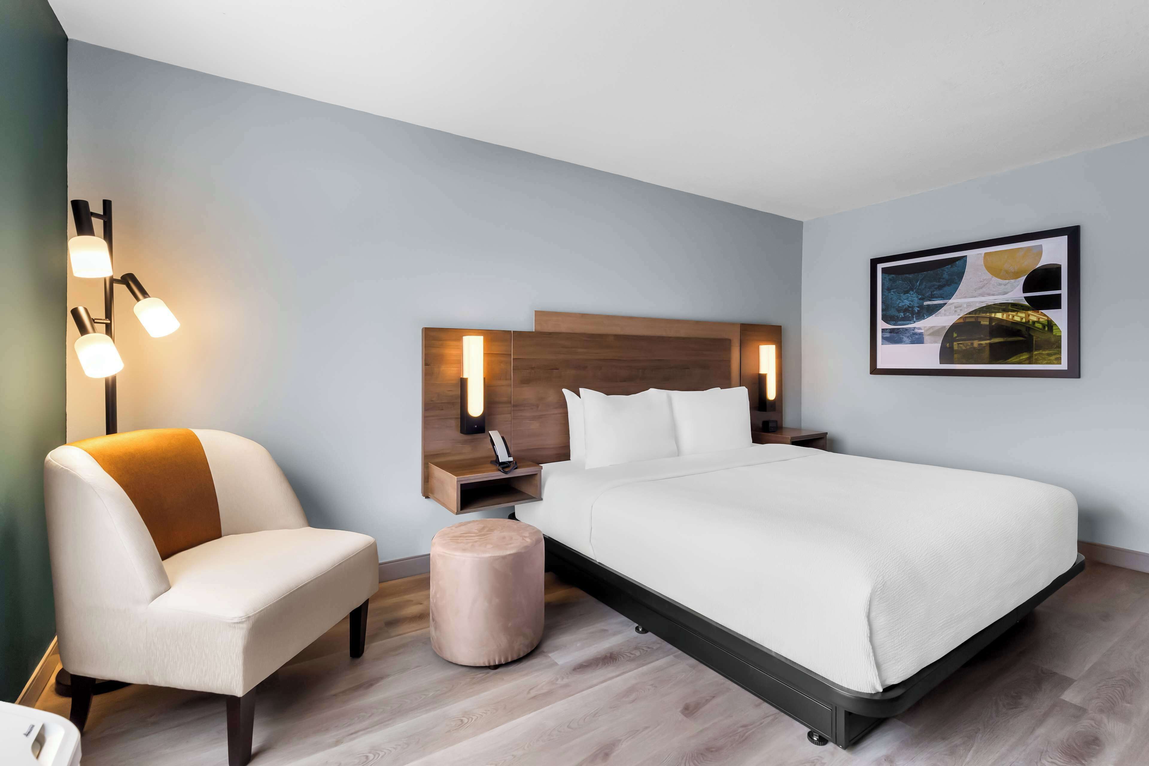 Una habitación de hotel moderna con una cama grande, una mesita de noche, una silla y una lámpara fijada a la pared.