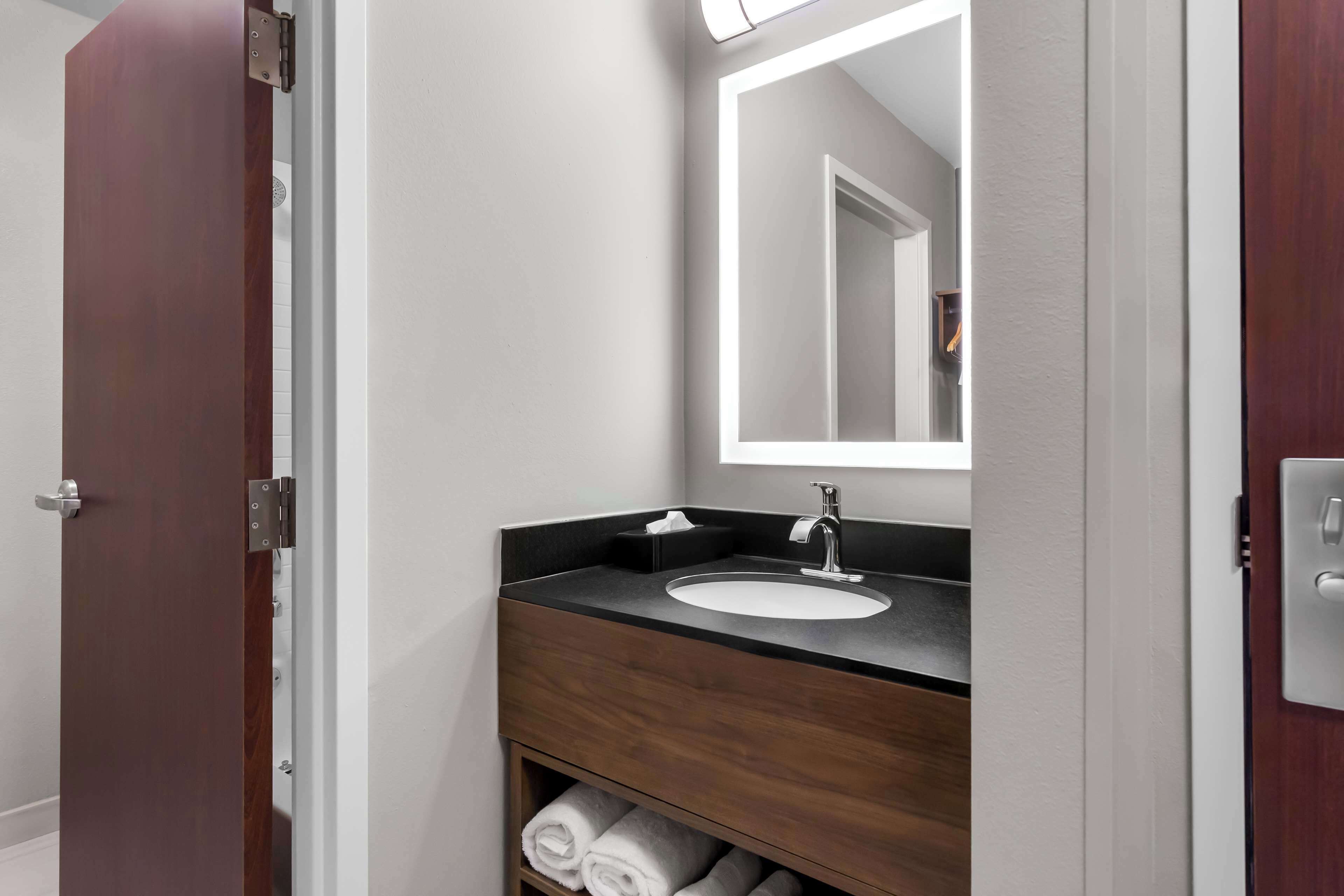 A modern bathroom with a dark wood vanity, white sink, and a mirror with integrated lighting.