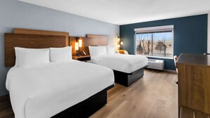 Habitación de hotel con dos camas, un escritorio y ventana con vistas a árboles.