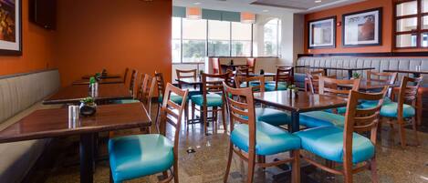 Un interior de restaurante con cabinas y mesas, sillas con cojines azules y cuadros en las paredes.