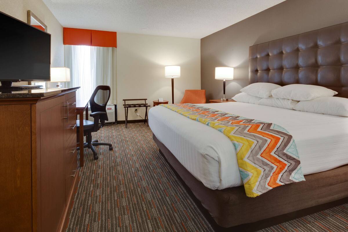 Una habitación de hotel con una cama grande, un escritorio con silla, televisión y dos lámparas de noche.