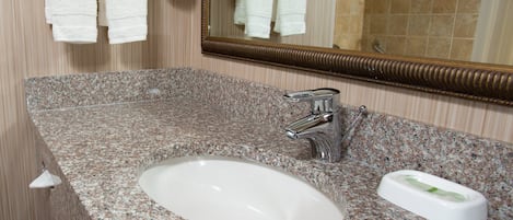 A bathroom with a granite countertop, a white sink, a mirror, and white towels hanging on a towel rack.