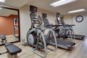 Un gimnasio con cintas de correr, elípticas y una banca.