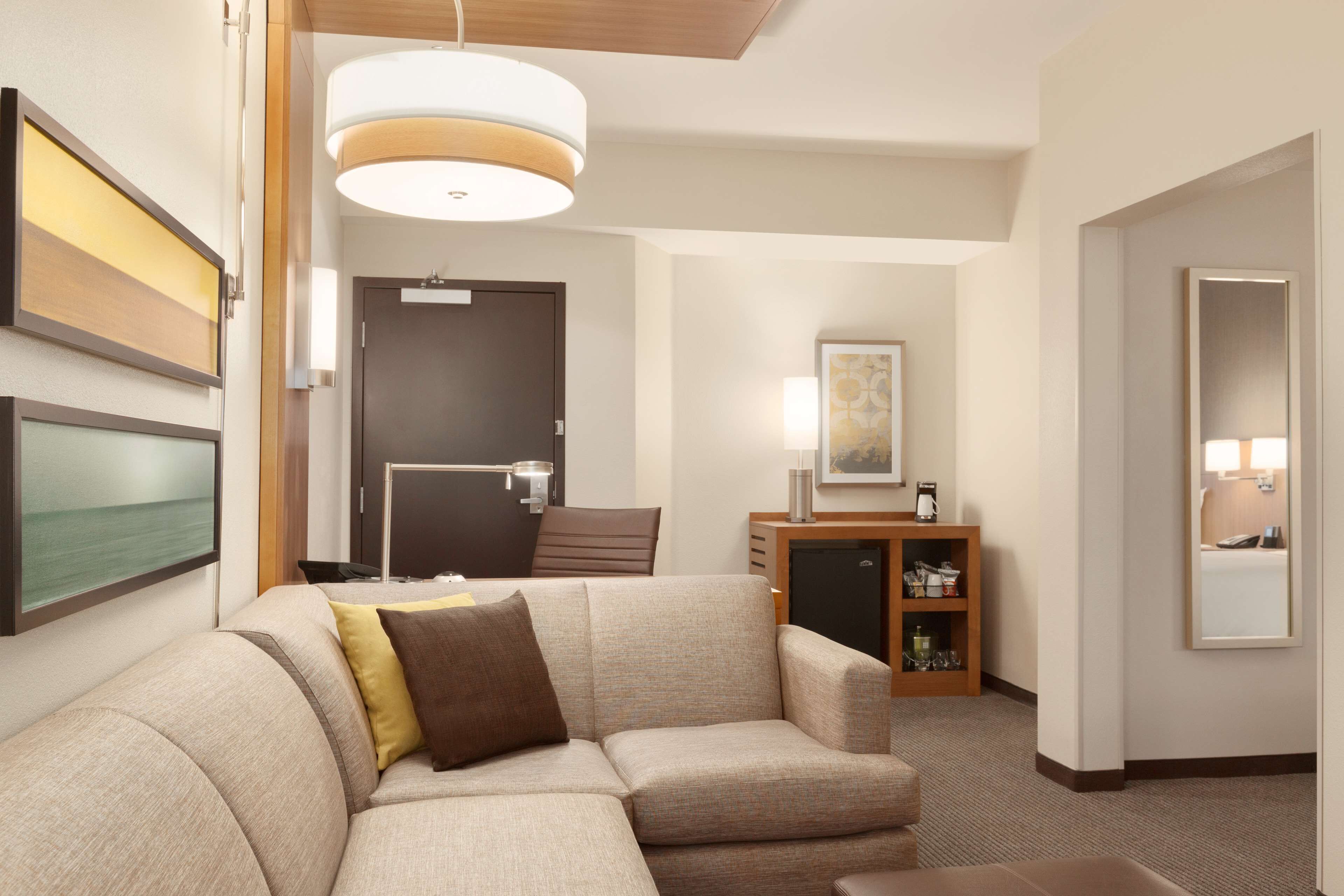 Habitació d'hotel moderna amb un sofà modular, un moble de bany amb vetreria, un escriptori i un mirall gran.