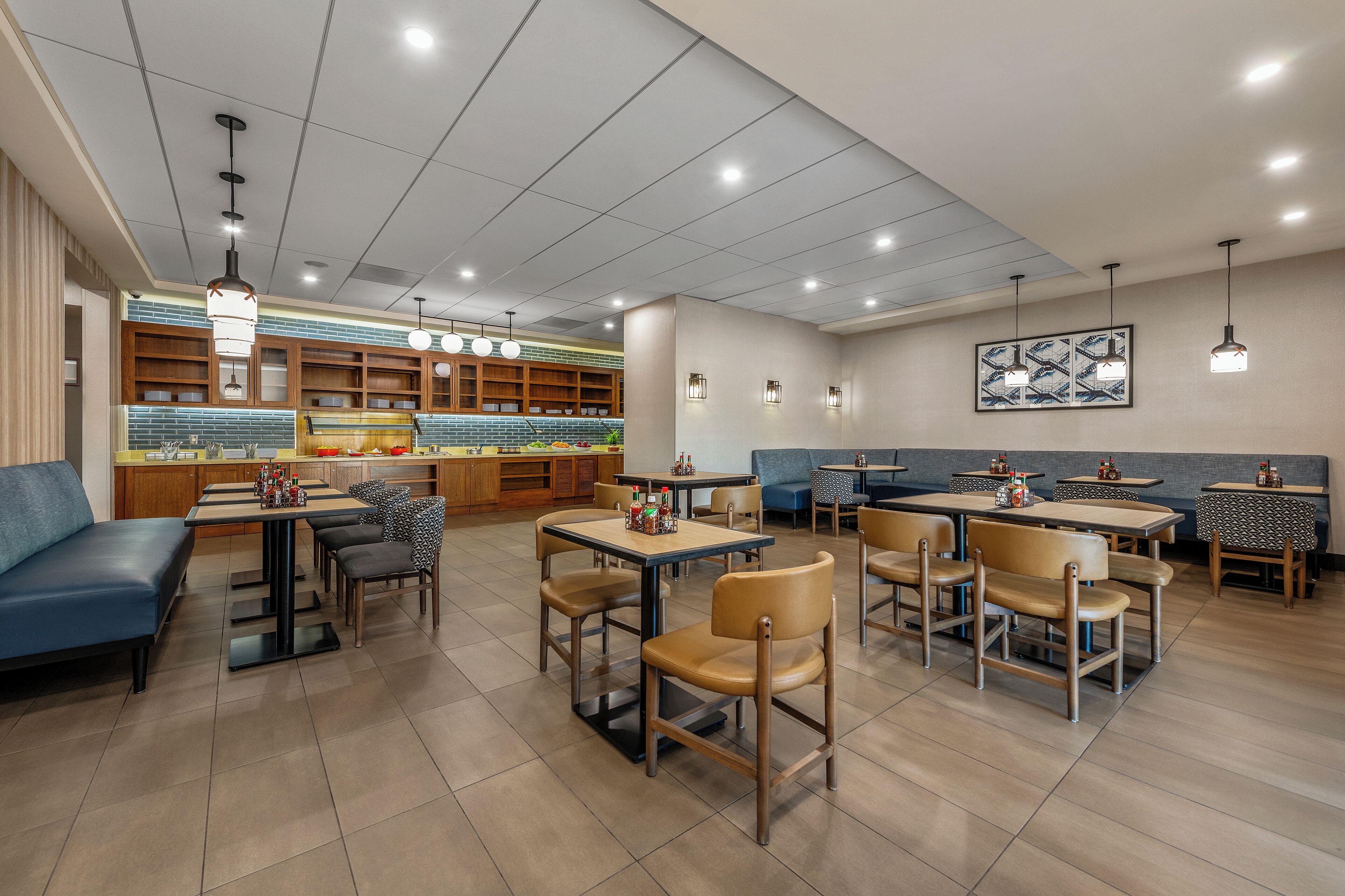 A modern restaurant with a clean layout, featuring a mix of dining tables and booths, wooden chairs, and a visible kitchen area.