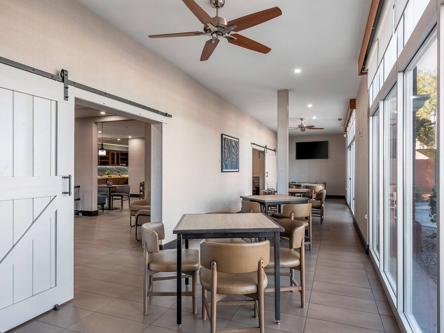A spacious dining area with high ceilings, a ceiling fan, and large windows offering views of the outdoors.