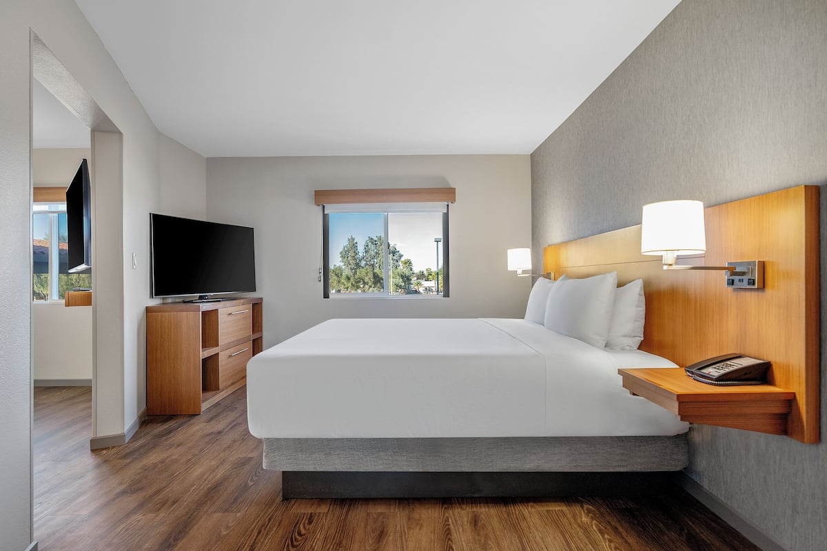 A modern hotel room with a large bed, wooden nightstands, a flat-screen TV, and a window with a city view.