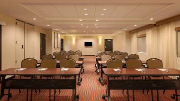 A conference room with tables, chairs, and a television screen.