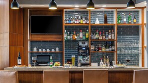 A bar area with a TV, shelves of liquor bottles, a coffee machine, and three leather chairs. - Hyatt Place Phoenix/Chandler-Fashion Center (Chandler)