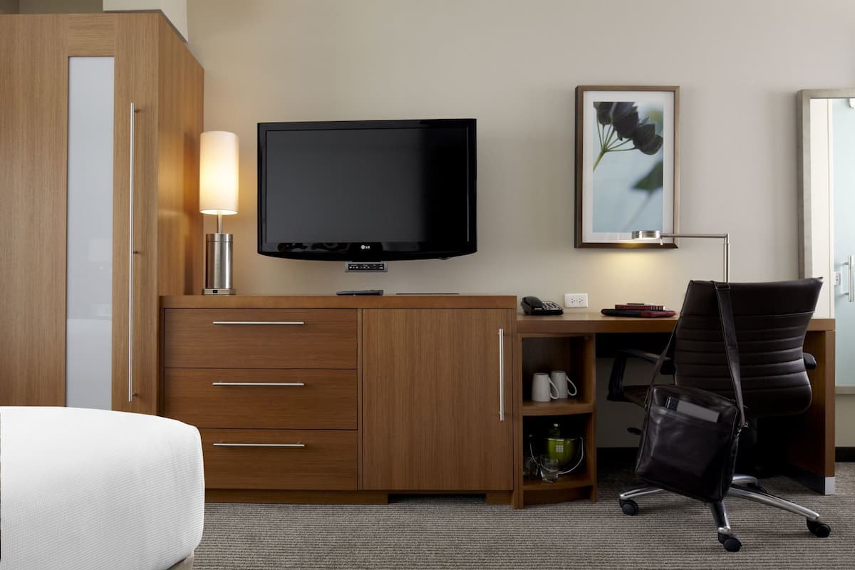 A hotel room with a wooden desk, a television, a chair, a lamp, and a framed picture on the wall.