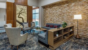 A modern lobby with a stone wall, a sofa, two armchairs, a coffee table, and a floor lamp. - Hyatt Place Phoenix/Chandler-Fashion Center (Chandler)