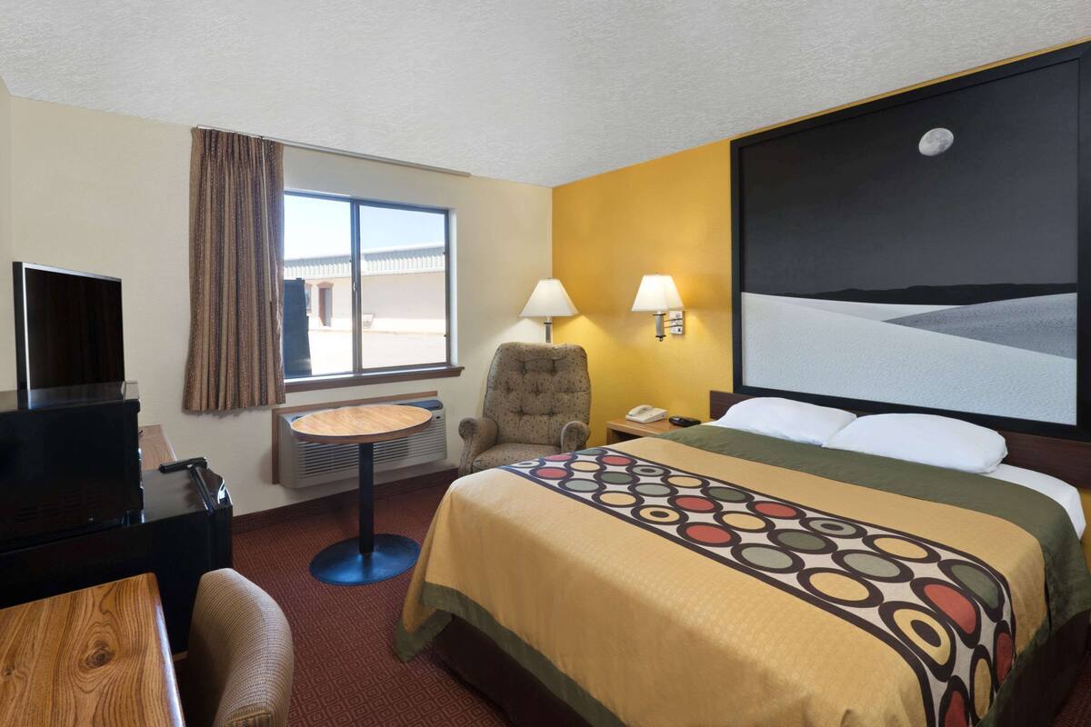 Une chambre d’hôtel avec un lit, un bureau, une chaise, une télévision, une fenêtre et un tableau au mur.