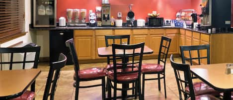A restaurant with wooden cabinets, a red wall, and a counter with various food items and a coffee machine.