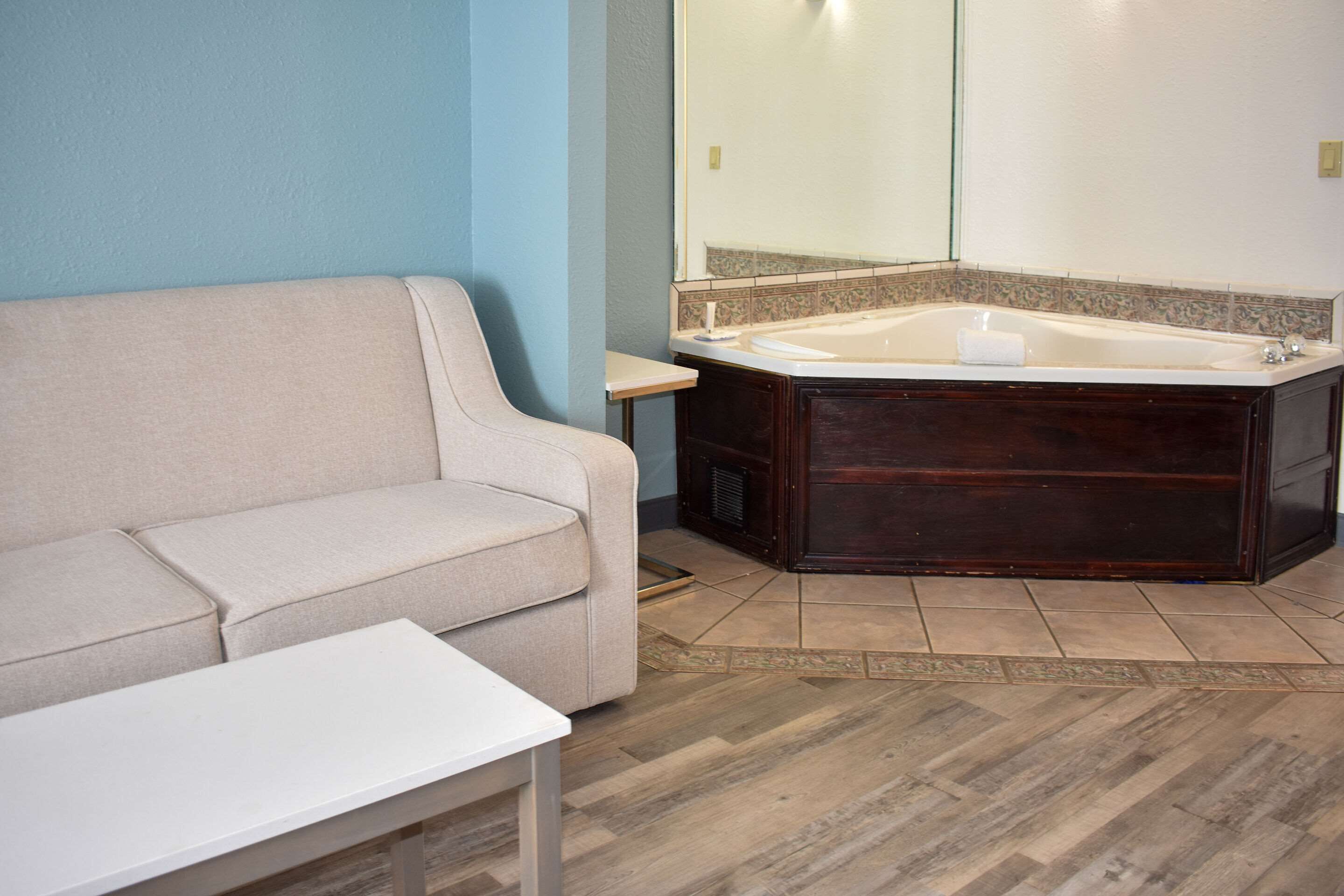 Un baño con un sofá color beige, una mesa blanca y una bañera grande.