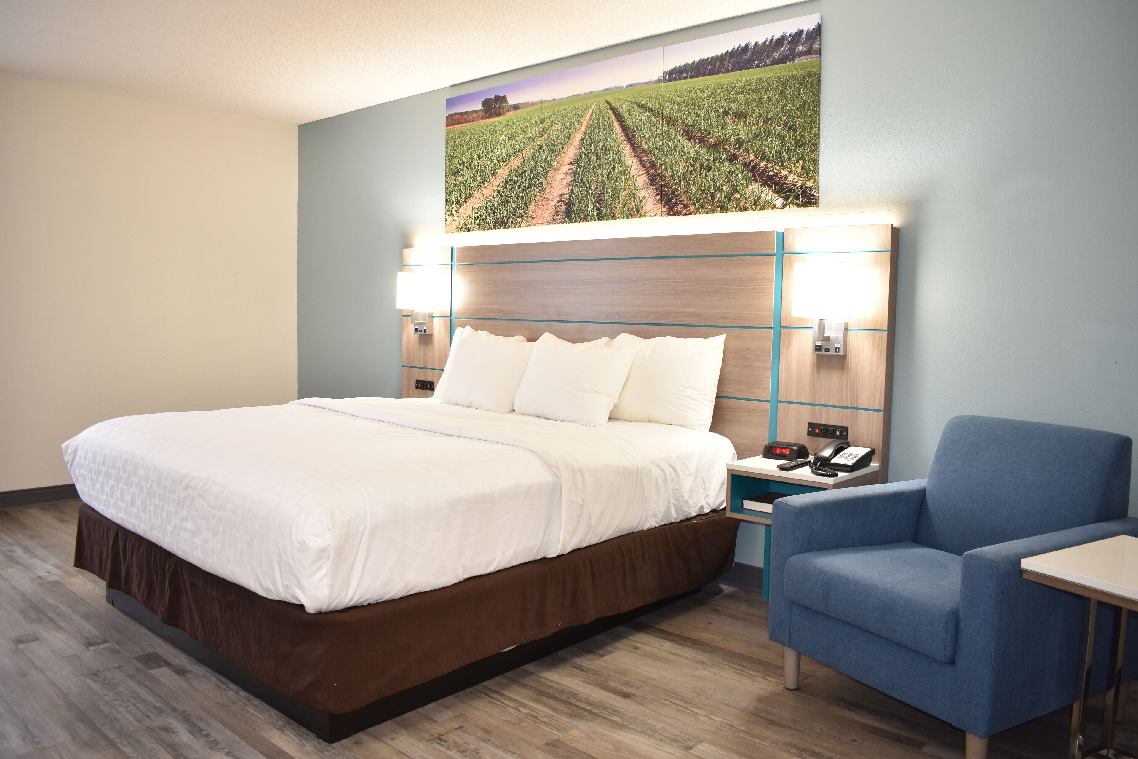 A hotel room with a large bed, a blue armchair, a small table, and a wall-mounted telephone.