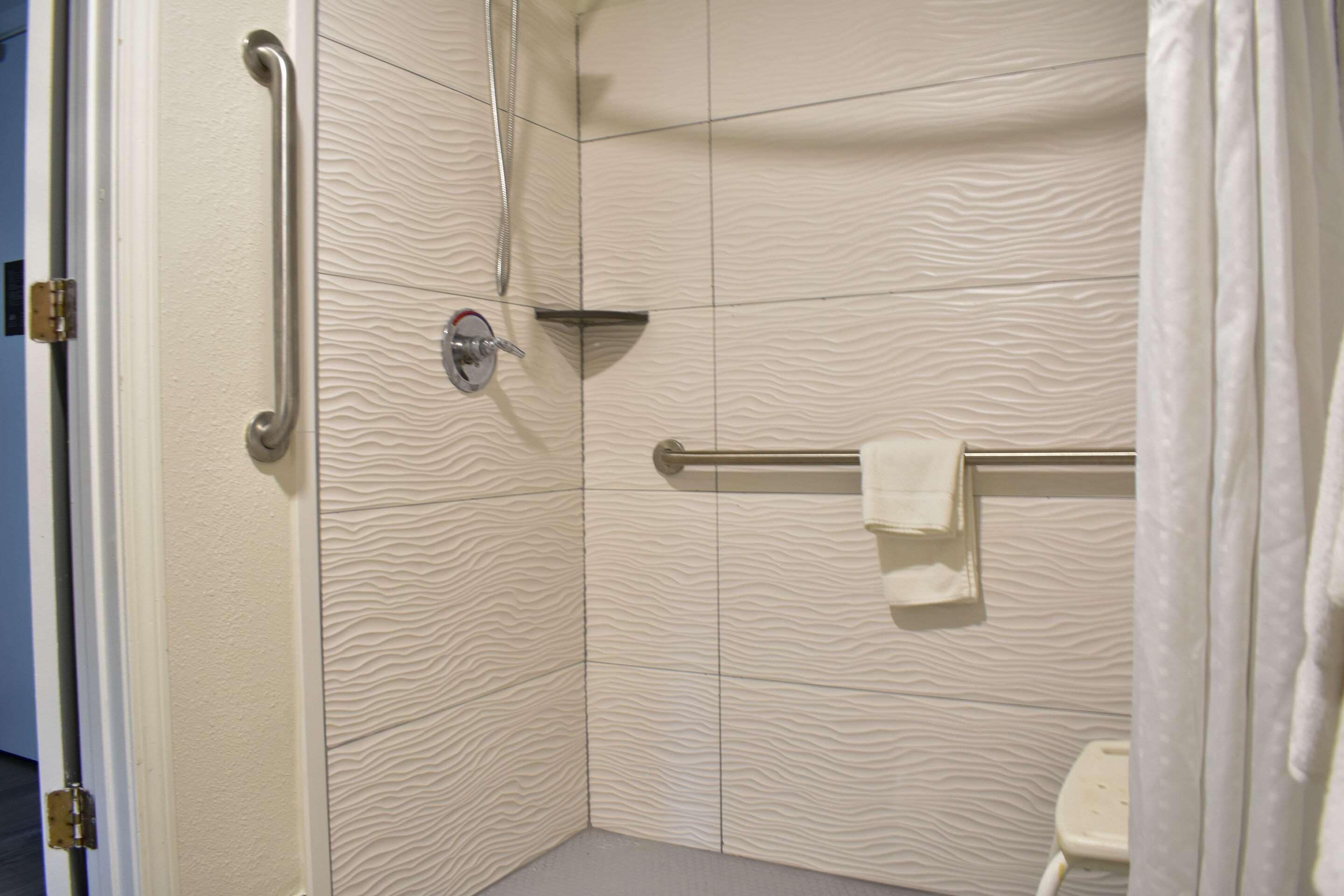 Une salle de bain avec des murs à texture, une barre d’appui, un porte-serviettes et un rideau de douche.