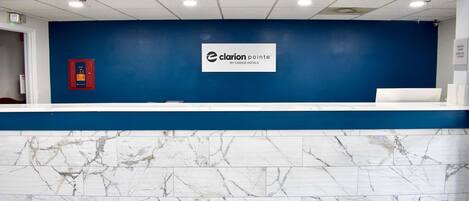 Un área de recepción con pared azul, mostrador de mármol y un letrero que dice "Clarion Pointe by Choice Hotels".
