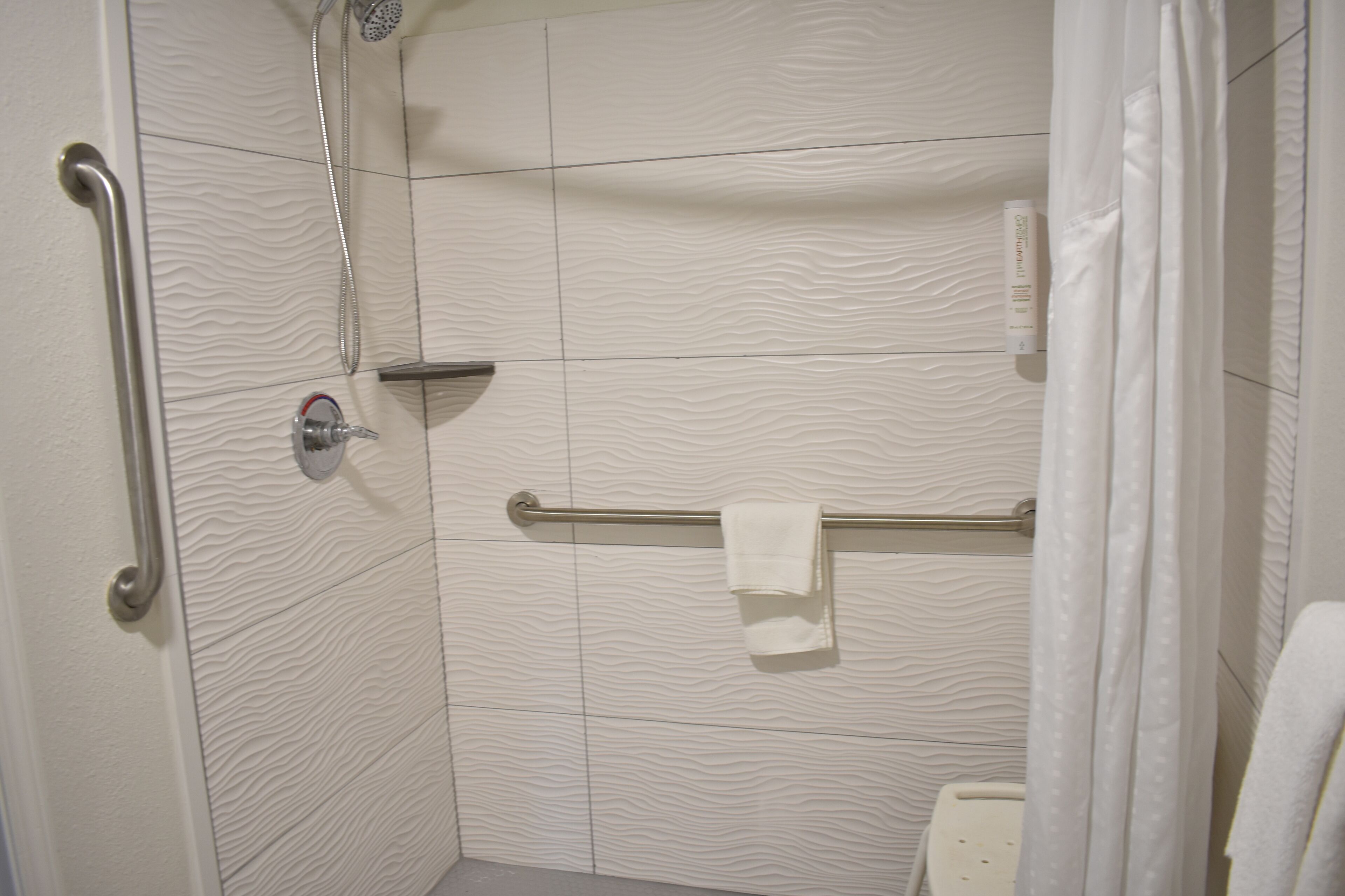 A shower with a handrail, a towel rack, and a showerhead.