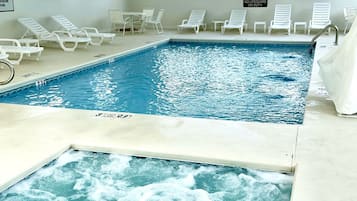An indoor swimming pool with multiple lanes, lounge chairs, and a hot tub area.