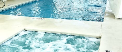 An indoor swimming pool with multiple lanes, lounge chairs, and a hot tub area.
