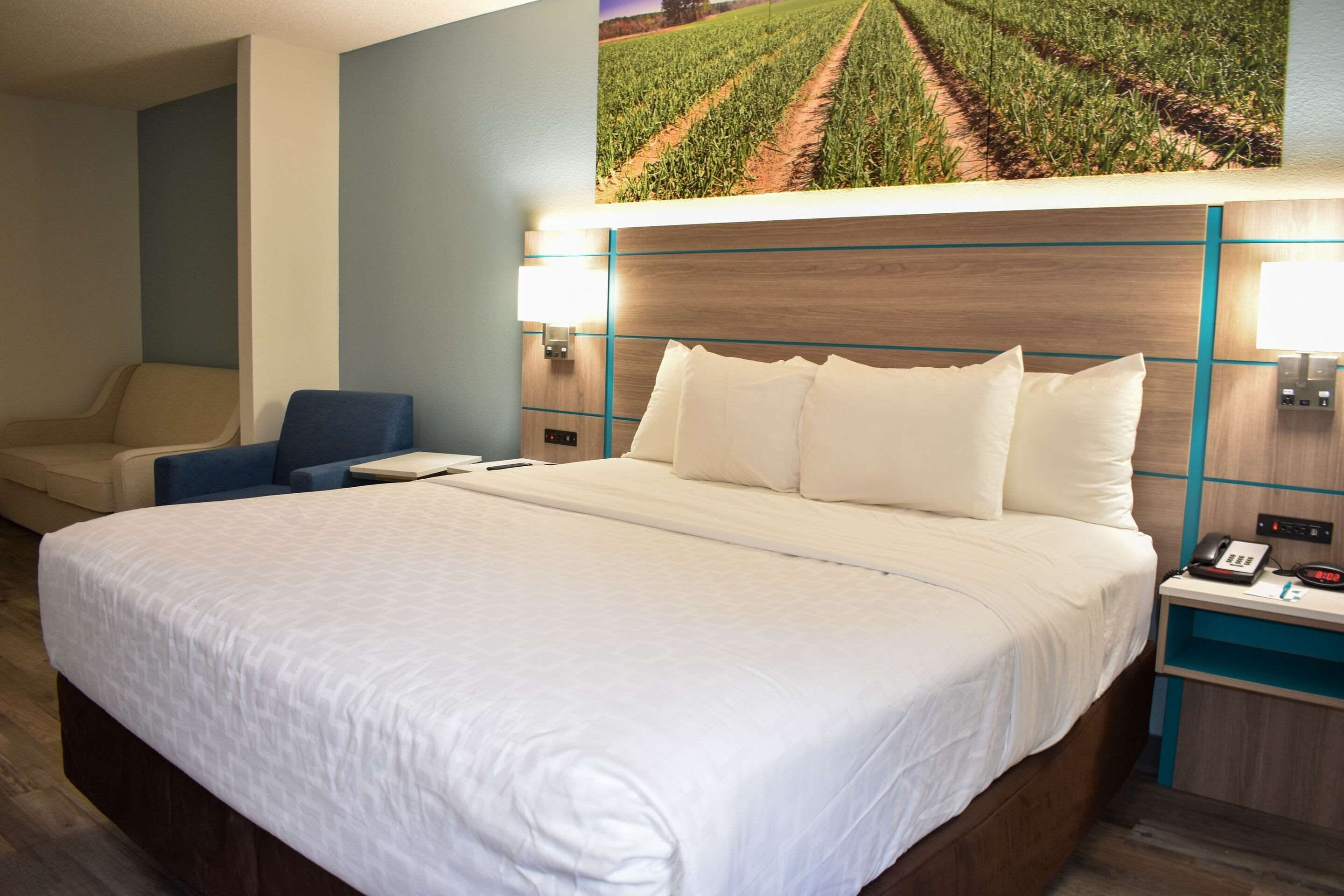 Habitación de hotel con una cama grande, una silla, una mesita de noche con teléfono e iluminación en la pared.