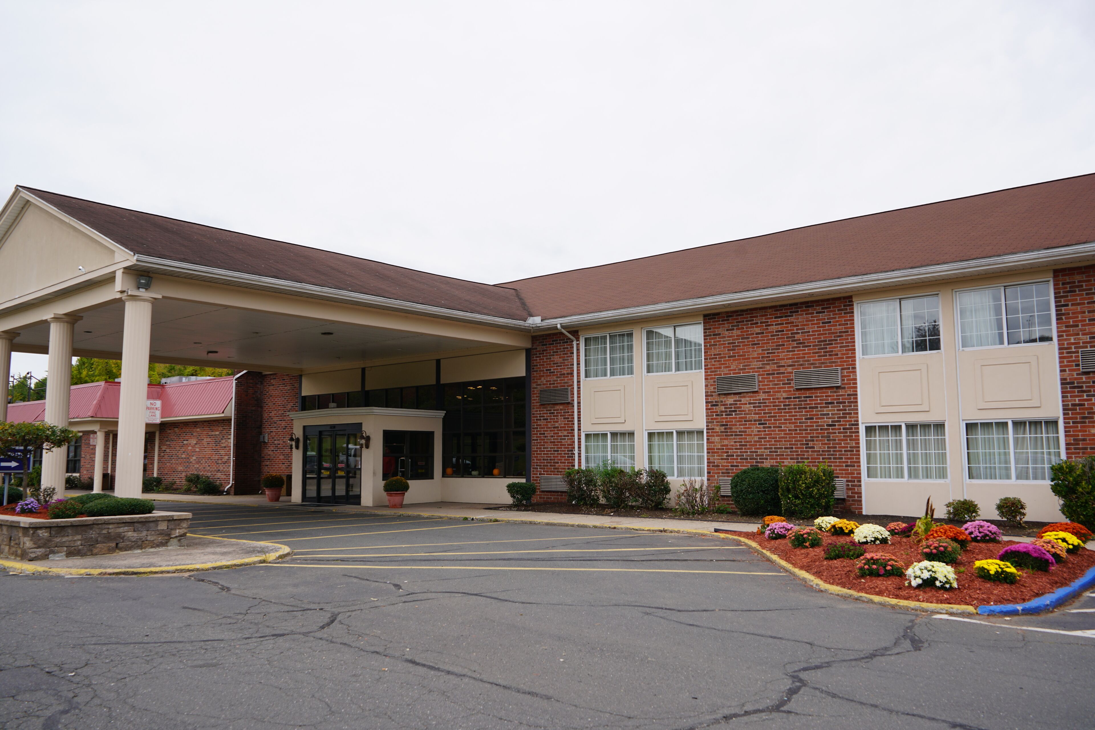 A two-story building with a covered entrance, brick facade, and a parking lot with flower beds.