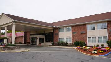 A two-story building with a covered entrance, brick facade, and a parking lot with flower beds.