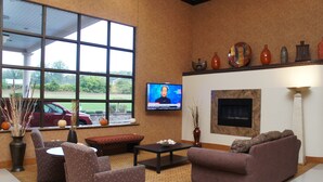 A living room with a fireplace, comfortable seating, a television, and a view of the outdoors. - Rodeway Inn & Suites East Windsor (East Windsor)