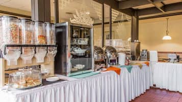 A buffet setup with clear glass containers of various food items, a buffet table with white tablecloths, and a decorative glass panel with a floral design.