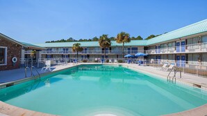 A pool area with a clear blue pool, lounge chairs, and a building with multiple balconies and palm trees. - Motel 6 Tifton, GA (Tifton)