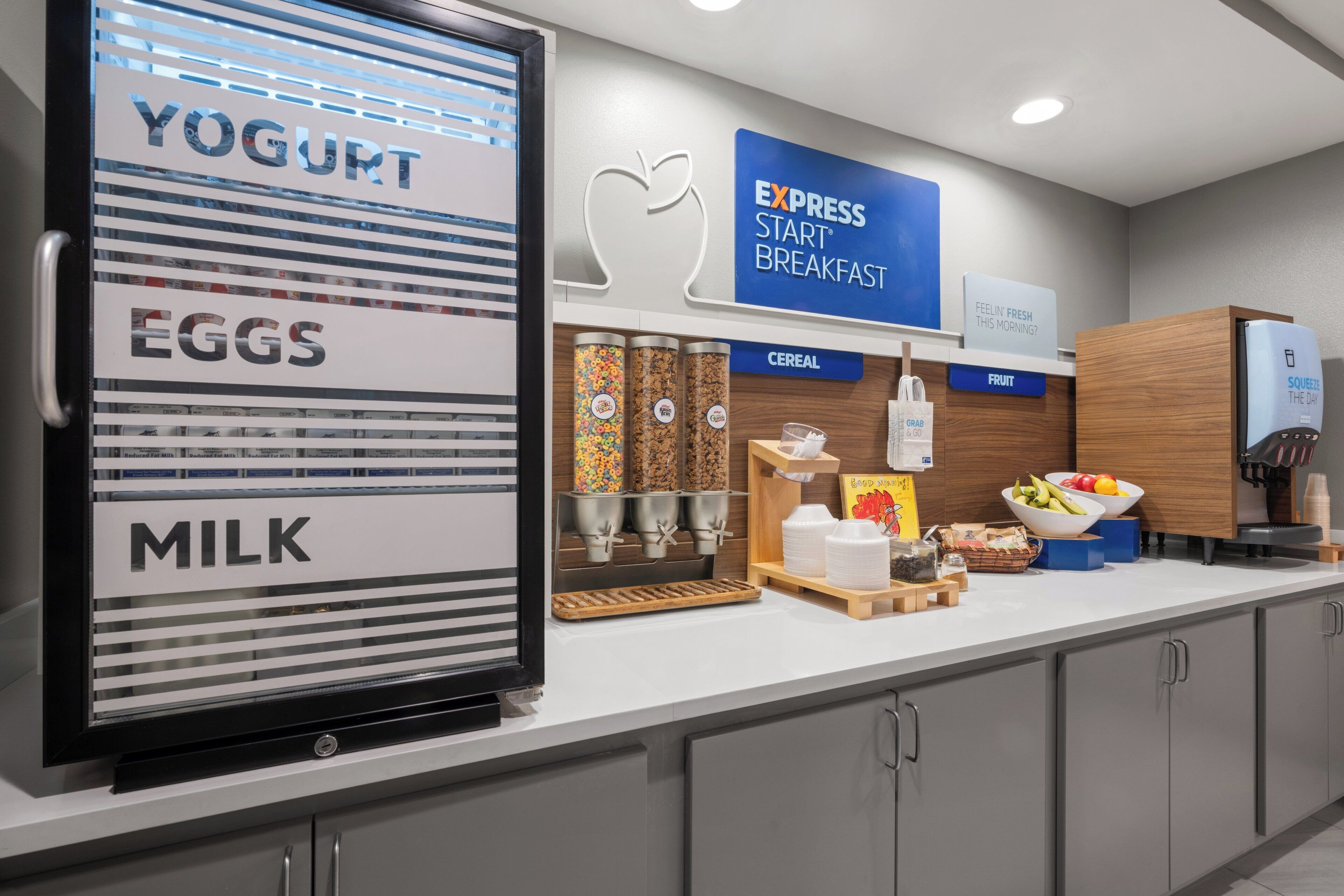 Una barra de desayuno moderna con dispensadores etiquetados para yogur, huevos y leche, y un cartel que anuncia Desayuno Express.
