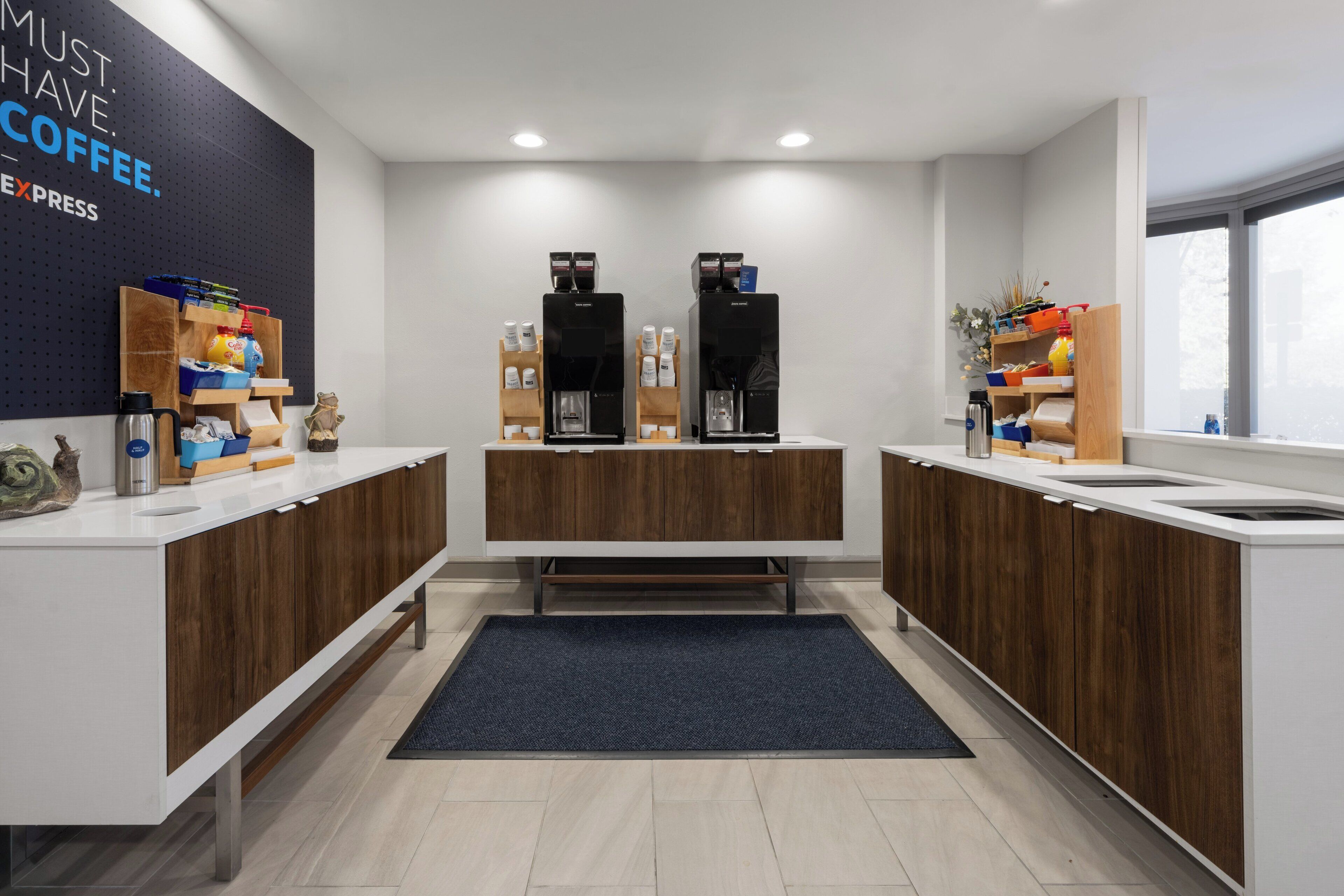 A modern kitchen with two coffee machines, wooden cabinets, and a blue rug.