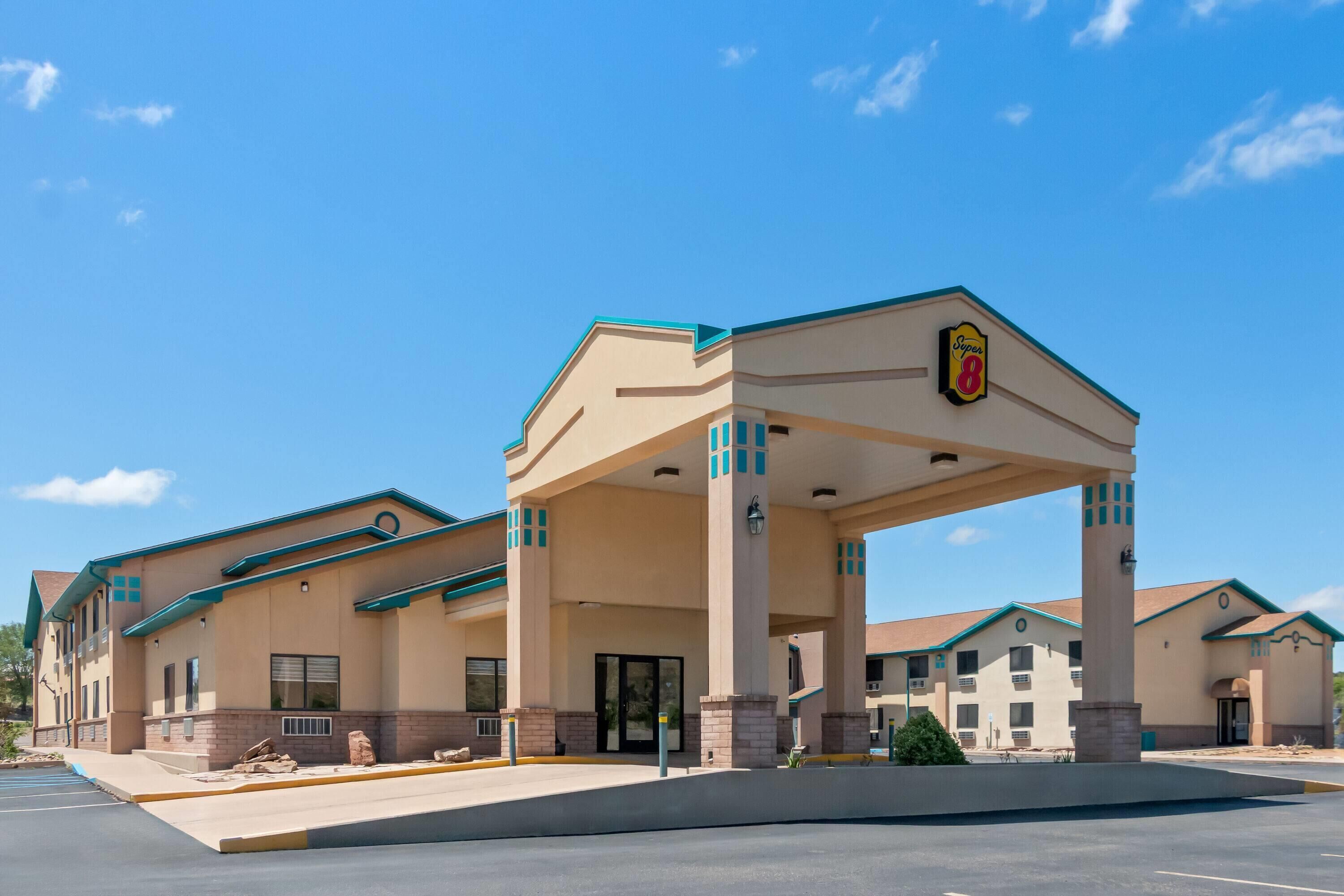 A hotel with a central entrance, multiple balconies, and a parking lot.