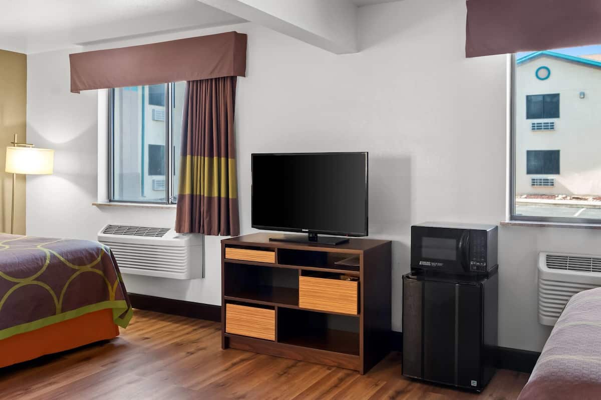 Ein Hotelzimmer mit Bett, Fernseher, Minikühlschrank und einem Fenster mit Vorhängen.