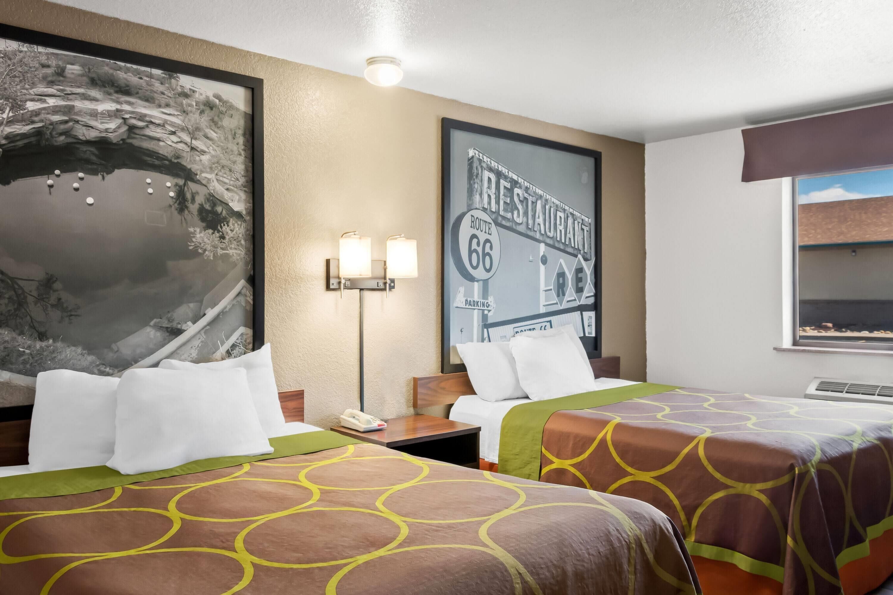 A hotel room with two beds, a large framed picture of Route 66, and a wall-mounted lamp.