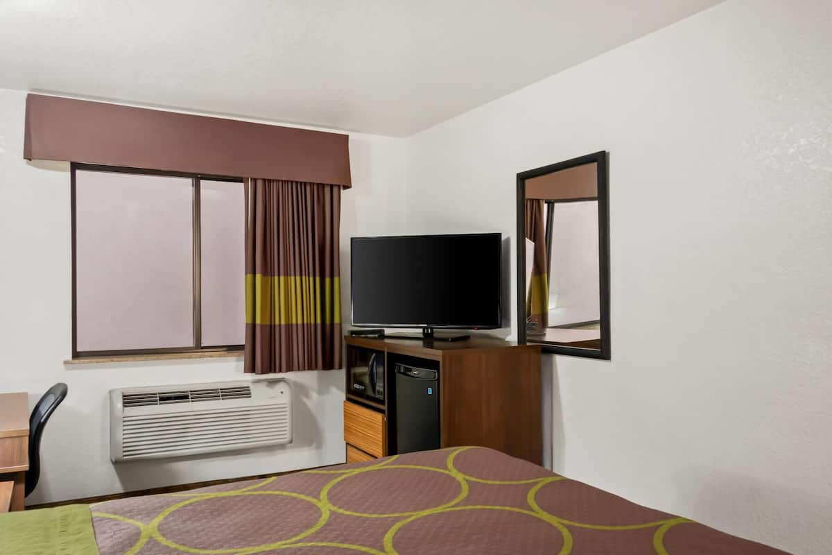 Ein Hotelzimmer mit einem Bett, einem Schreibtisch, einem Sessel, einem Fernseher, einer Heizung und einem Fenster mit Vorhängen.