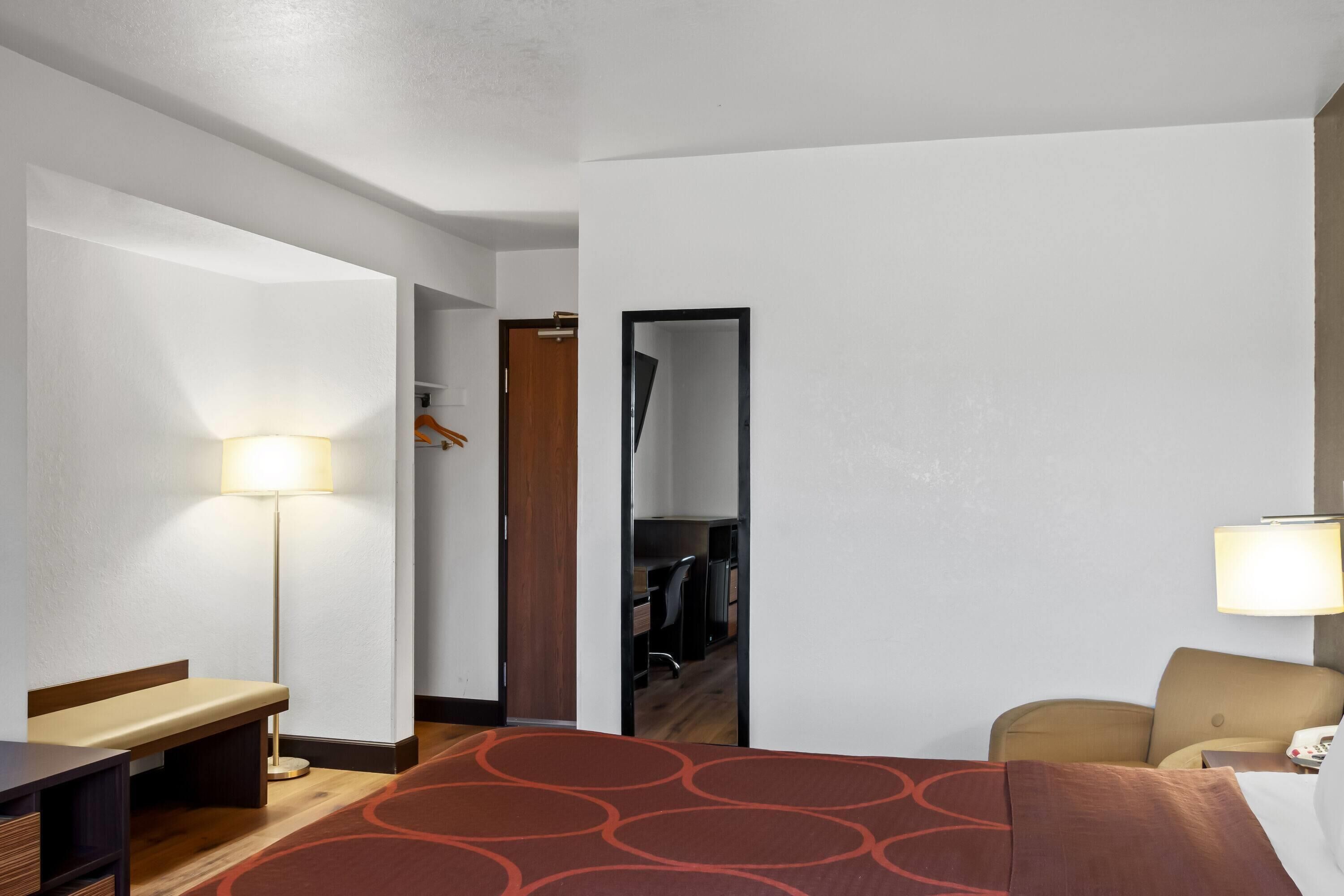 Una habitación de hotel con una cama, un escritorio, una silla, una lámpara y un armario.