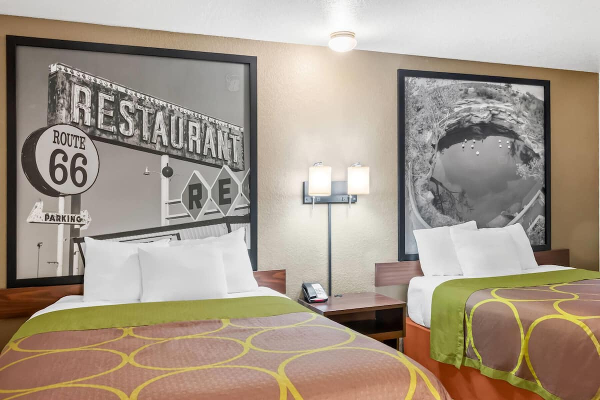 Ein Hotelzimmer mit zwei Betten, einem Schild für das Route 66 Restaurant, einer Lampe und einem Bilderrahmen mit einem Teich.