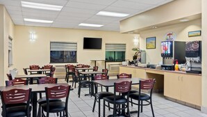 A restaurant with multiple tables and chairs, a counter with a beverage dispenser, and a television mounted on the wall.