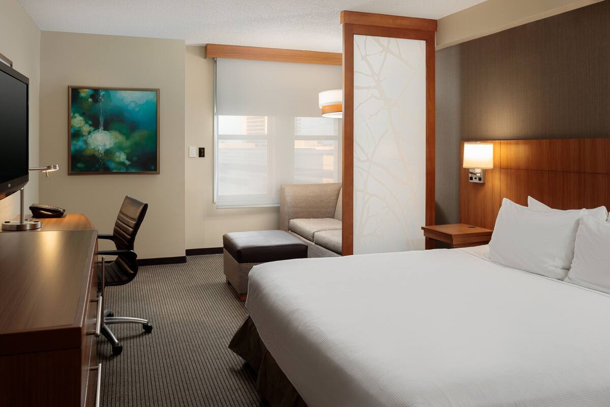 A hotel room with a large bed, a desk with a chair, a sofa, and a TV.