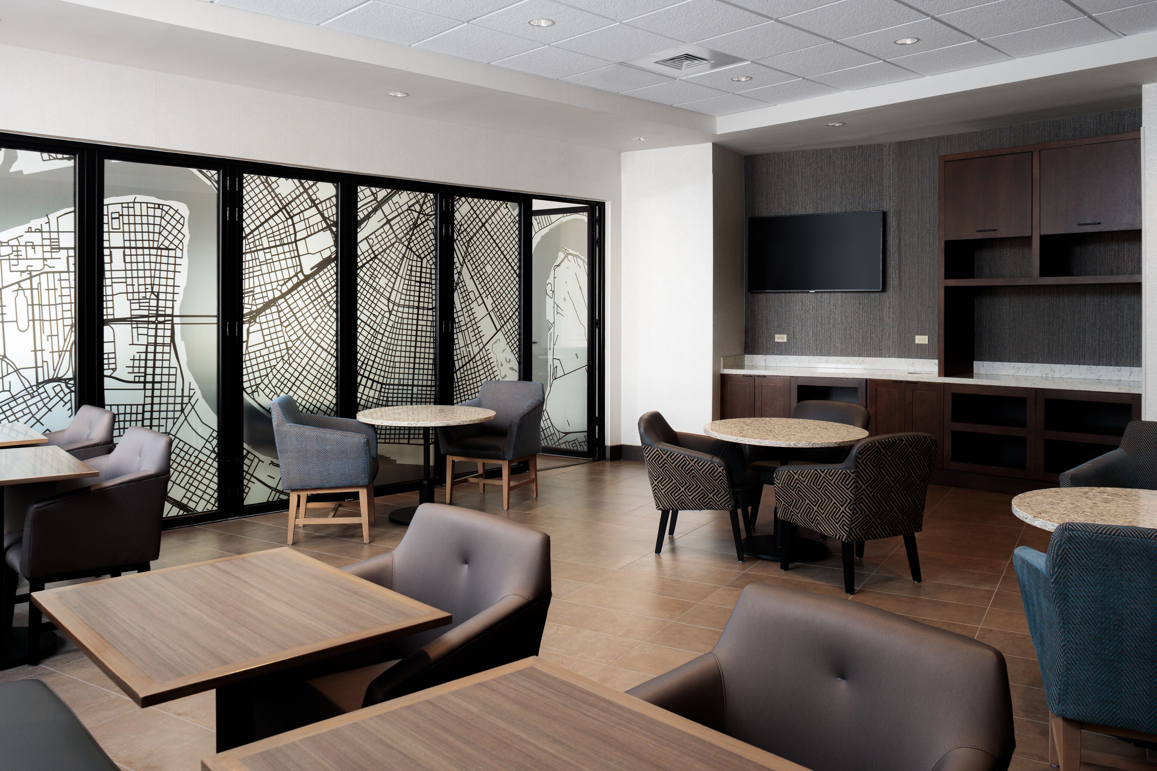 A modern interior with round tables and chairs, a large wall map, and a flat-screen TV.